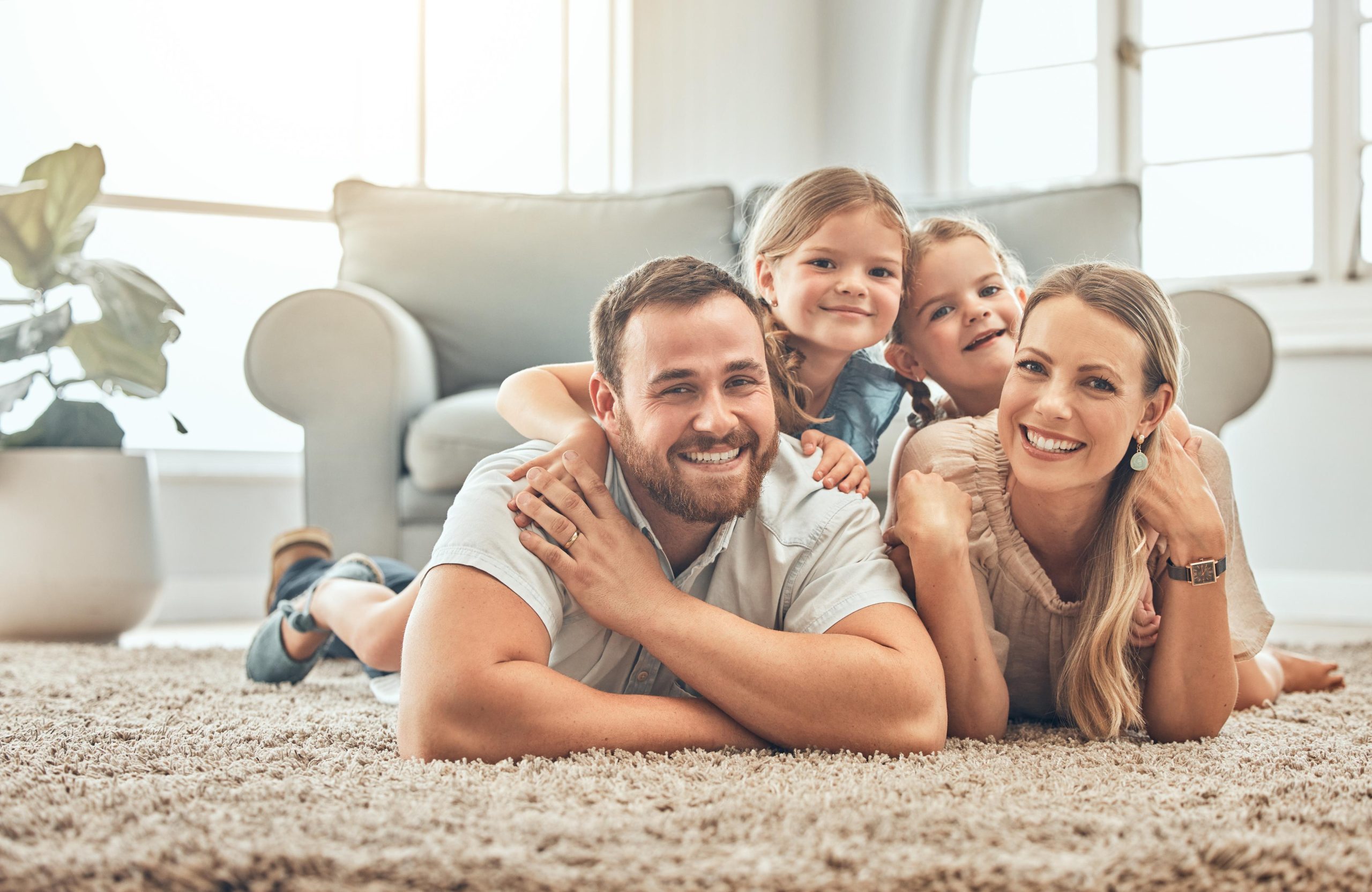 Young family in the living room at home. Portrait of an affectionate and happy family lying on the floor of the lounge. Spending quality time together. A mother, father and two sisters at home American northeast 2 story house in summer with red siding and beautiful green grass